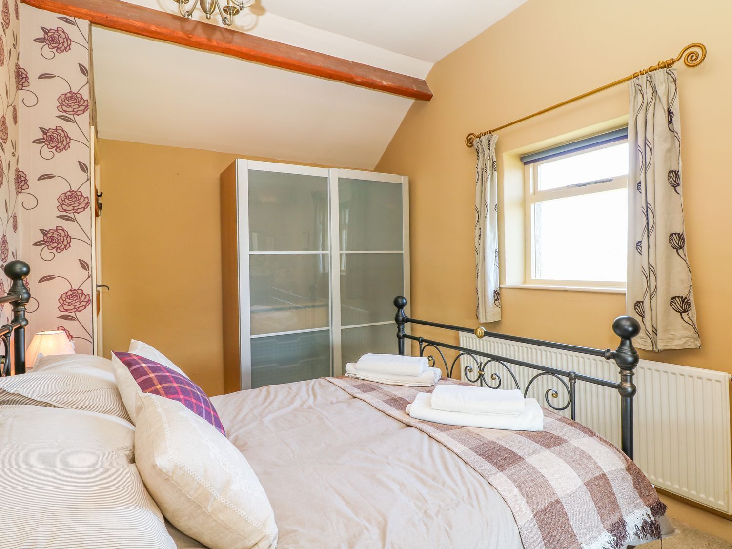 A bedroom with a bed, a wardrobe, a window with curtains, and a radiator.