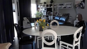 Een moderne woonkamer met een ronde eettafel, zwart-wit stoelen, een bank en een boekenkast.