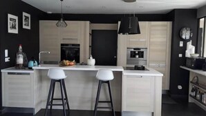Een moderne keuken met een centraal eiland, twee barkrukken, een zwarte hanglamp en een zwarte deur.