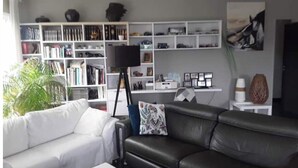 Een moderne woonkamer met een witte bank, een leren bank in zwart en een boekenkast vol boeken en decoratieve objecten.