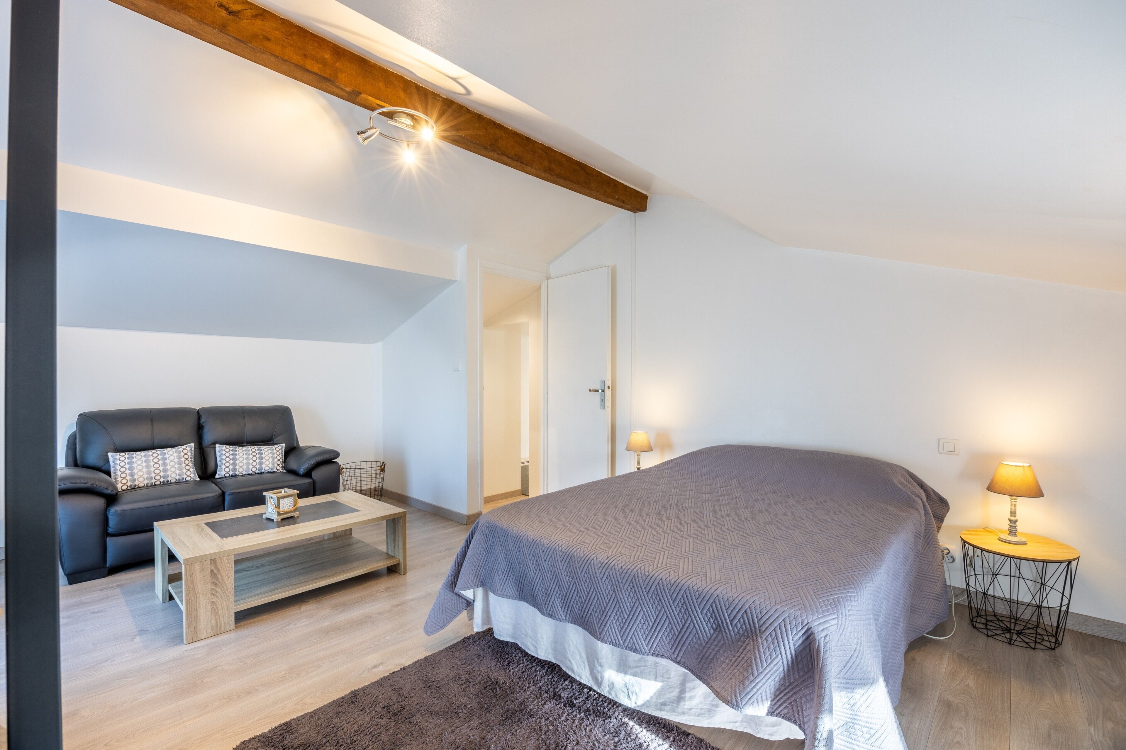 A bedroom with a bed, a sofa, a coffee table, a lamp, and a door.
