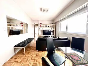 A compact living space with a sofa, a glass table, a bench, and a TV on a shelf. - -Belgrano- (Buenos Aires)