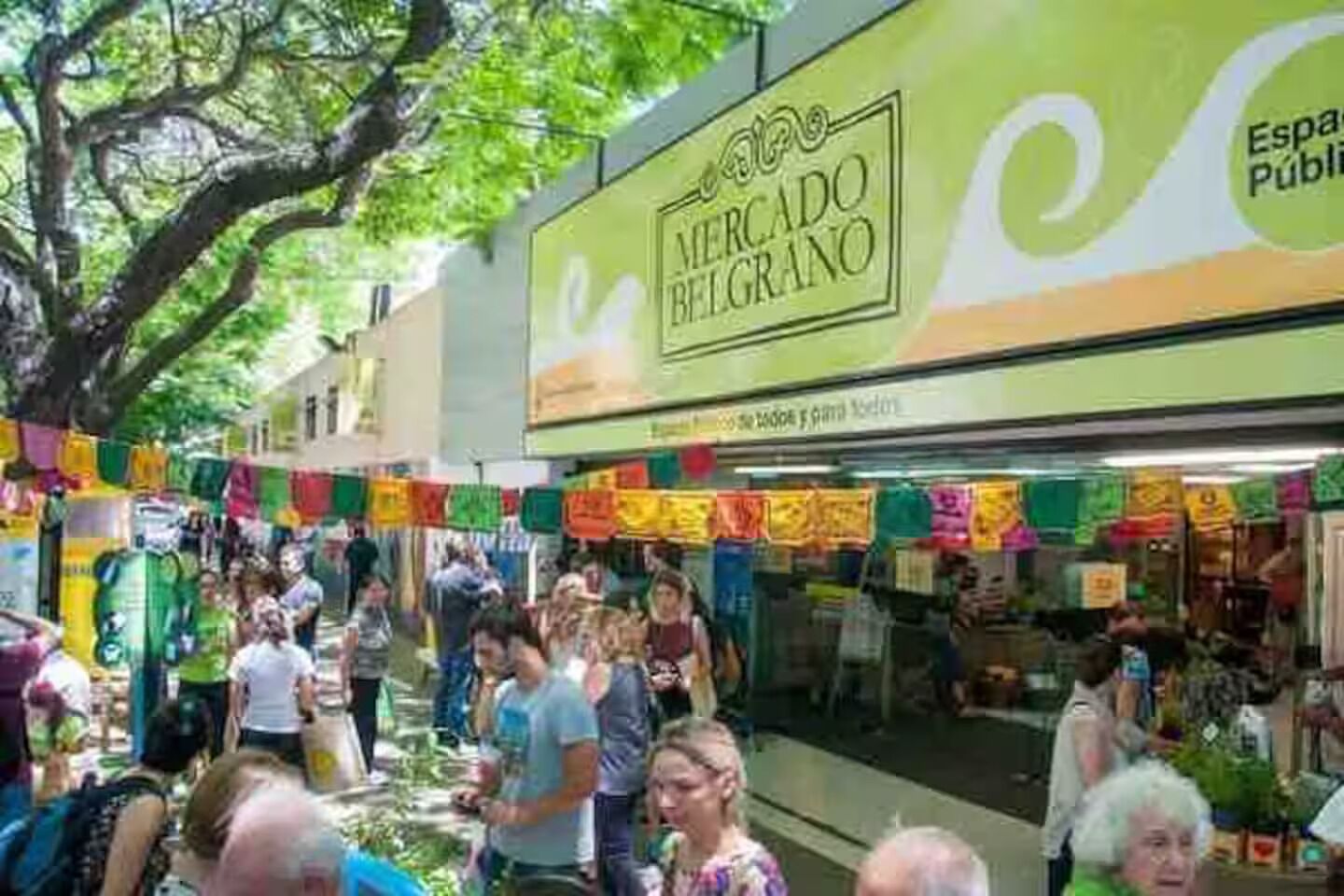 Um mercado ao ar livre movimentado com uma placa de destaque para o Mercado Belgrano.