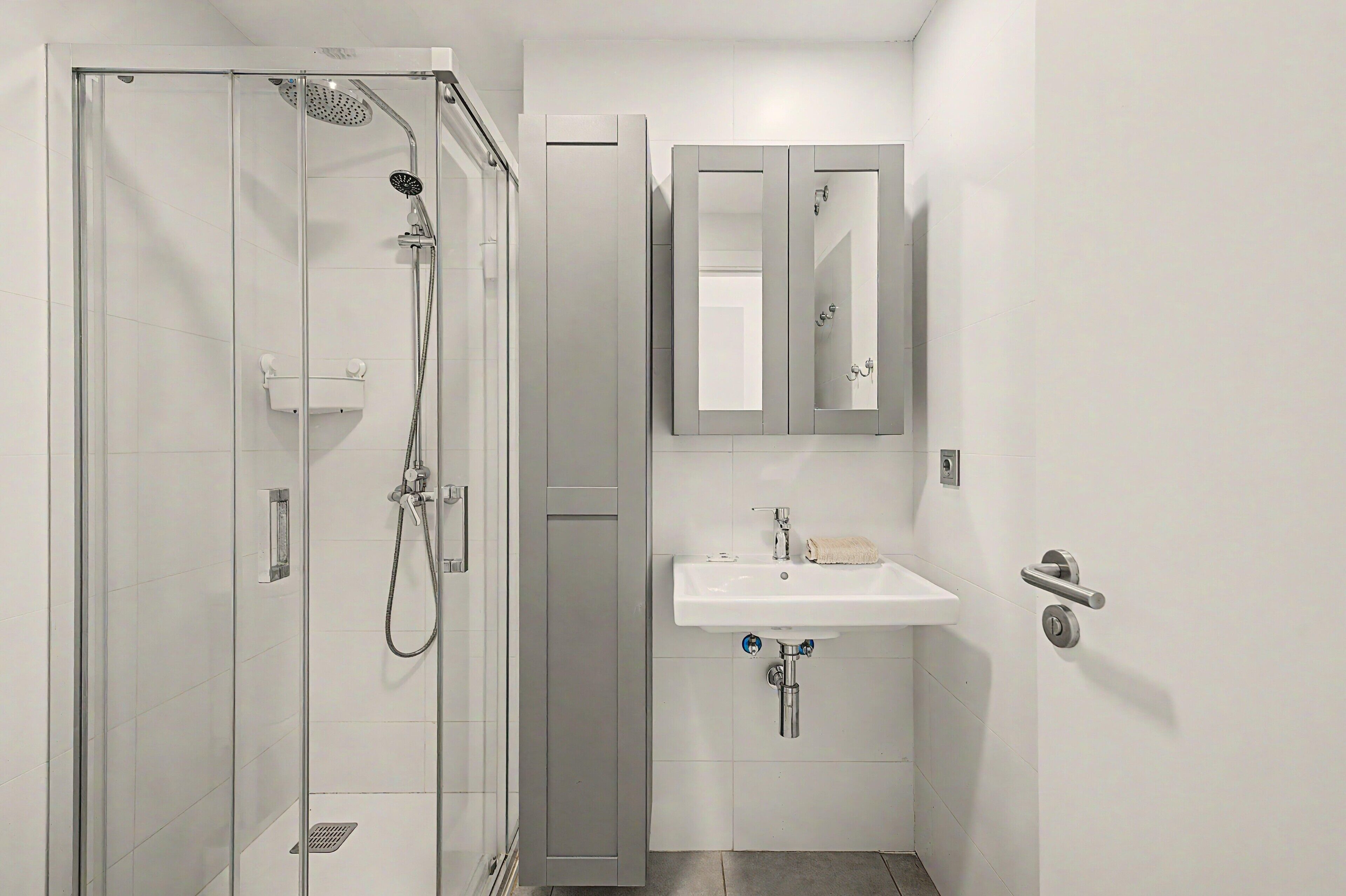 Ein modernes Badezimmer mit einer gläsernen Dusche, einem Waschbecken mit Spiegel darüber und einem Handtuchhalter.