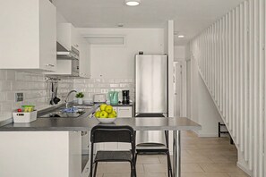 Een moderne keuken met een centraal eiland, roestvrijstalen apparatuur en een zithoek met twee stoelen.