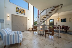 Una zona d'estar àmplia amb un sofà a ratlles, una taula de dinar amb caires i una escala amb barana.