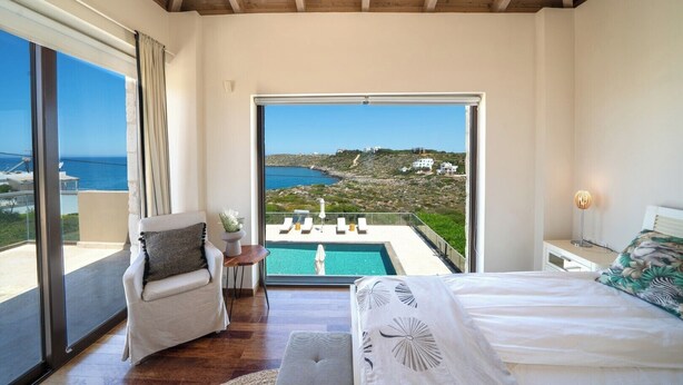 Quarto com uma janela ampla, cama, cadeira e vista para uma piscina e paisagem.