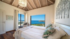 Quarto com cama grande, vista para o mar e teto de madeira.