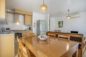 Een moderne keuken met houten kastjes, een eettafel met stoelen, een koelkast en hanglampen.