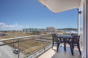 A balcony with a table and chairs, overlooking a modern building and a train track. - Apartment 'Campo Mar - T1 Com Piscina' with Sea View, Wi-Fi and Air Conditioning (São Martinho do Porto)