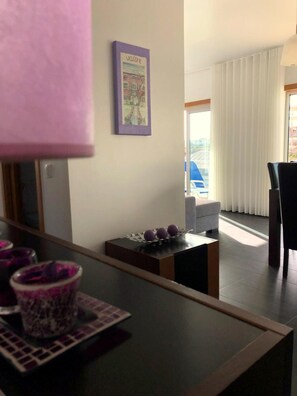 Ein modernes Hotelzimmer mit Blick nach außen, ein kleiner Tisch mit Dekoration, ein violettes Willkommensschild und ein Fenster mit Vorhängen.