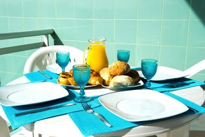 Ein gedeckter Tisch mit Tellern, Besteck, blauen Servietten, einer Kanne Orangensaft und Croissants.