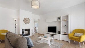 Una sala de estar moderna con un sofá, sillones, un televisor, una mesa de centro y una estantería.