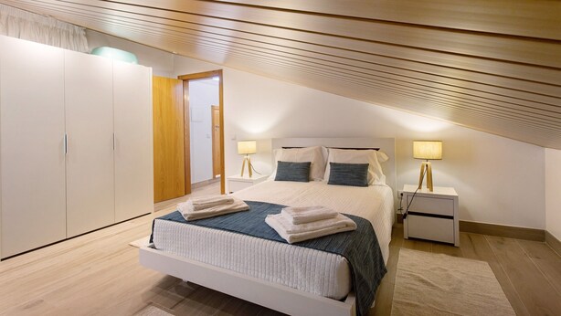 Un dormitorio con cama, mesitas de noche, armario y techo de listones de madera.