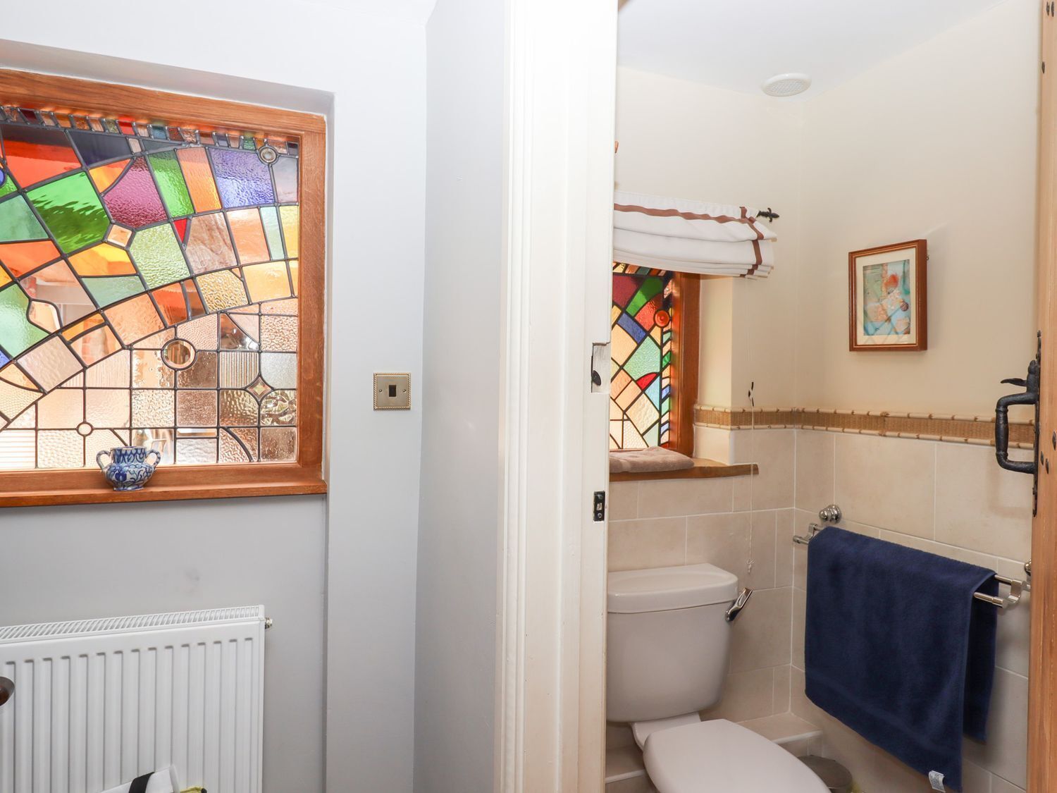 A bathroom with a stained glass window, a white toilet, a blue towel, and a small framed picture on the wall.