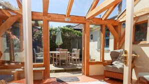 Una habitación iluminada por el sol, con un ventanal de vidrio que da al exterior, muebles de madera y una alfombra estampada.