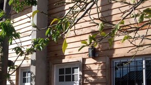 Uma casa de madeira com porta e janela brancas, cercada por árvores e um cercado de madeira.