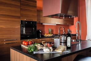 A modern kitchen with wooden cabinets, a black oven, stainless steel appliances, and fresh produce on the counter. - SUPERIOR APARTMENT OIL MILL VIEW (Matraia)