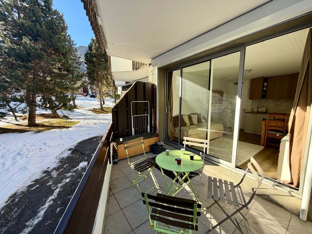 Ein Balkon mit Tisch und Stühlen, eine Glastür zu einem Zimmer und eine verschneite Landschaft mit Bäumen.