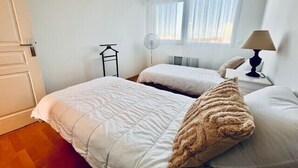 Una camera da letto con due letti, un comodino con lampada, una finestra con tende e un ventilatore a parete.