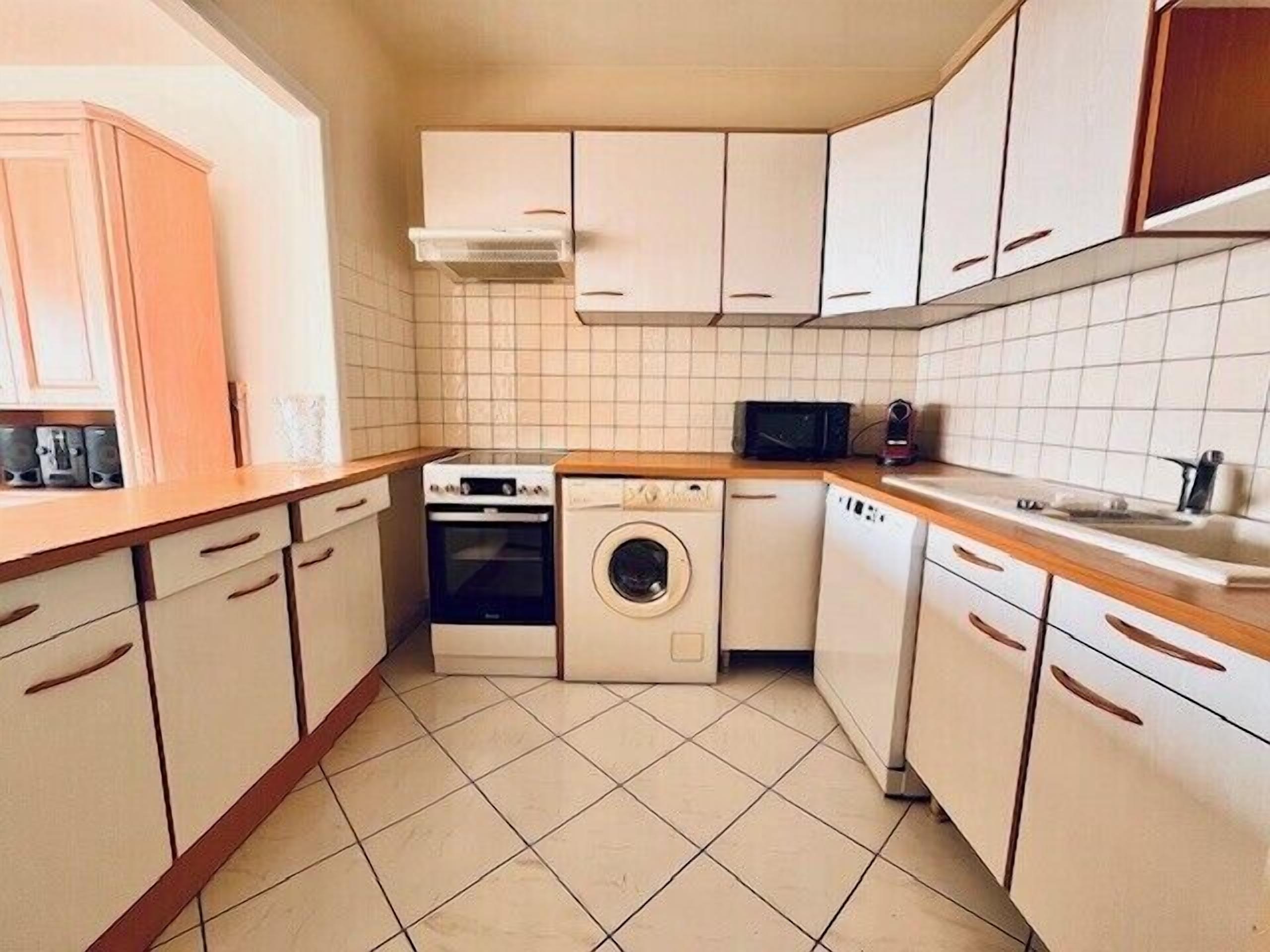 Une cuisine de taille réduite, avec des meubles blancs, un lave-linge, un four à micro-ondes et une cuisinière.