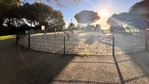 Un'area giochi recintata con uno sfondo soleggiato e alberi.