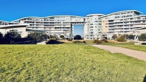 Un grande edificio a più piani con facciata curva, un ingresso centrale e un'area verde in primo piano.