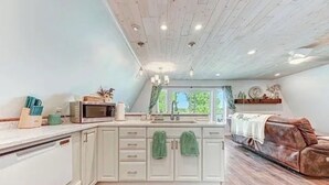 A kitchen with white cabinets, a microwave, and a sink. There is a brown leather sofa in the living area. - 3-bedroom waterfront cottage with unmatched views and dock on Tennessee River (Decatur)