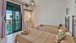 Un dormitorio con dos camas, un tocador, una mesita de noche, una lámpara, una lámpara colgante y vistas al exterior.