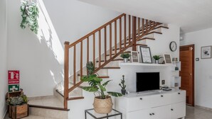 Una escalera con barandillas de madera, una consola blanca con televisor de pantalla plana y una planta en maceta.