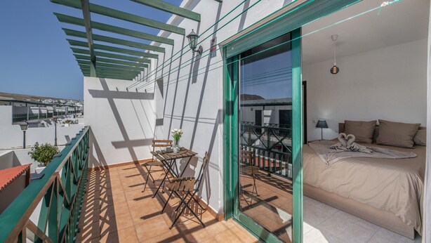 Un balcón con una mesa y sillas, una cama con una manta, y vistas de la ciudad.