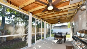 Un patio techado con ventilador de techo, una parrilla y una mesa con sillas.