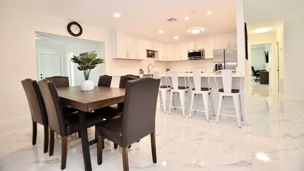 Una cocina moderna con gabinetes blancos, electrodomésticos de acero inoxidable y un comedor con mesa y sillas de madera.