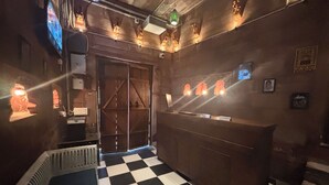 Een geruit vloerkleed, een houten deur en een receptiebalie met naambord.