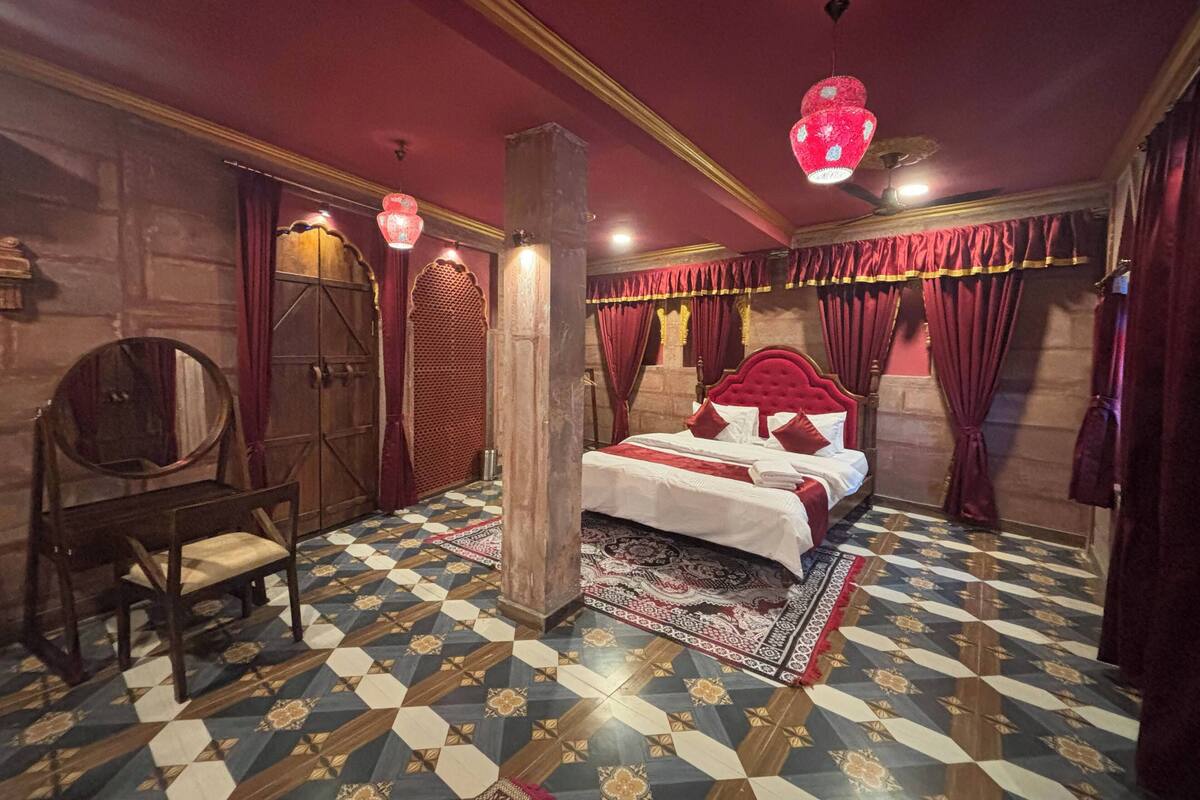Een kamer met een groot bed, een houten stoel, vloertegels met een patroon en rode gordijnen.