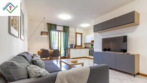 Een modern appartement met een grijze bank, een eethoek, een keuken met televisie en een balkon.