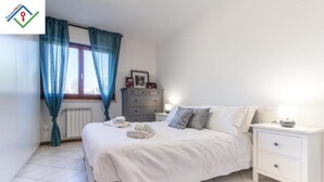 Een slaapkamer met een bed, nachtkastjes, een dressoir en een raam met gordijnen.