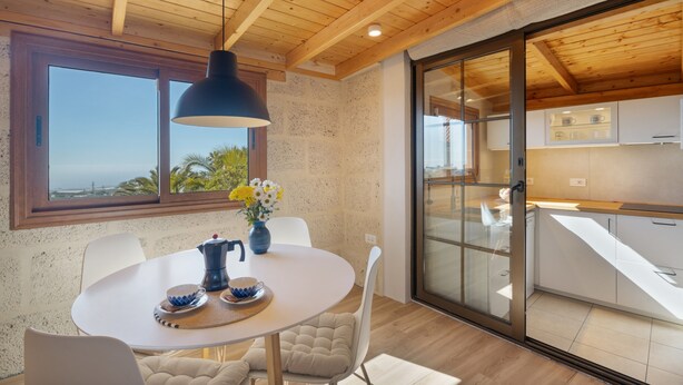 Una cocina moderna con armarios blancos, techo de madera y un amplio ventanal con vistas panorámicas.