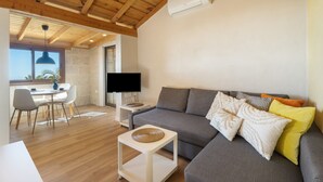 Una sala de estar moderna con un sofá gris, un televisor de pantalla plana, vigas de madera y un comedor con mesa y sillas.