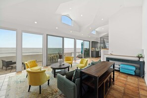 Amplia sala de estar con un ventanal grande que da al mar, una mesa de comedor de madera, sillones amarillos y un sofá.