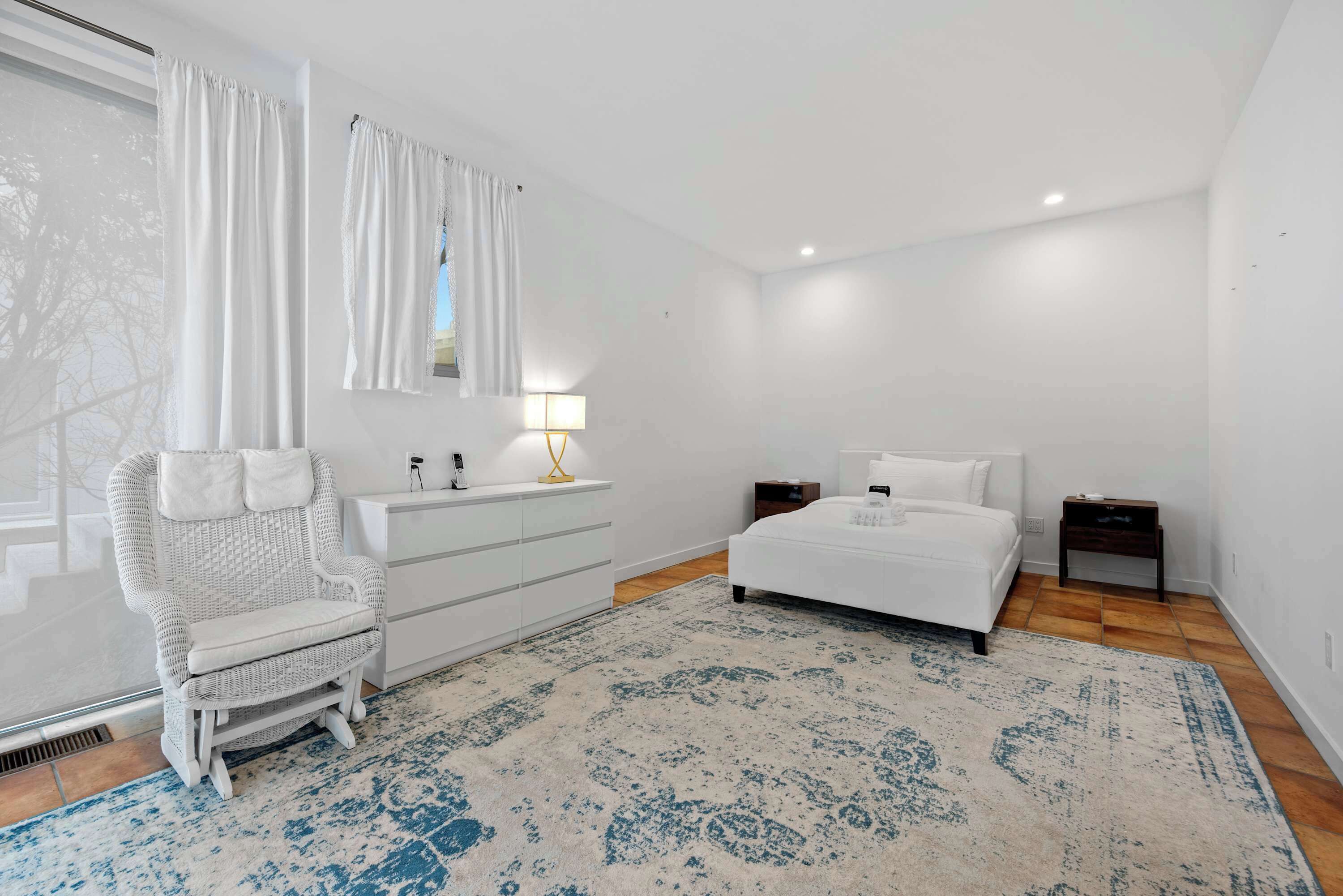 A bedroom with a bed, a dresser, a chair, a lamp, and a window with curtains.