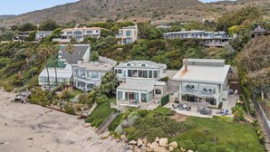 A hillside residential area with modern homes, a beach, and a mountain in the background.