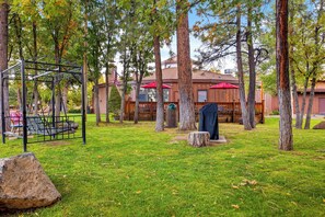 Un espacio al aire libre con césped, árboles, un columpio y un edificio con toldos rojos al fondo.
