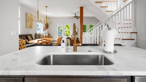 Una cucina moderna con isola centrale, lavello in acciaio inossidabile e zona pranzo con sedie e tavolo in legno.