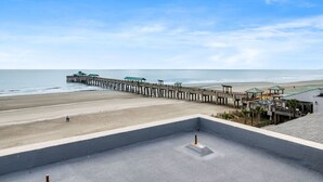Une vue sur la plage avec une jetée qui s’avance dans l’océan, une plage de sable et un bâtiment doté d’un toit plat.