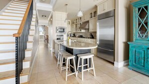 Une cuisine moderne dotée d’un îlot central, d’appareils électroménagers en acier inoxydable et d’un escalier avec des rampes en bois.