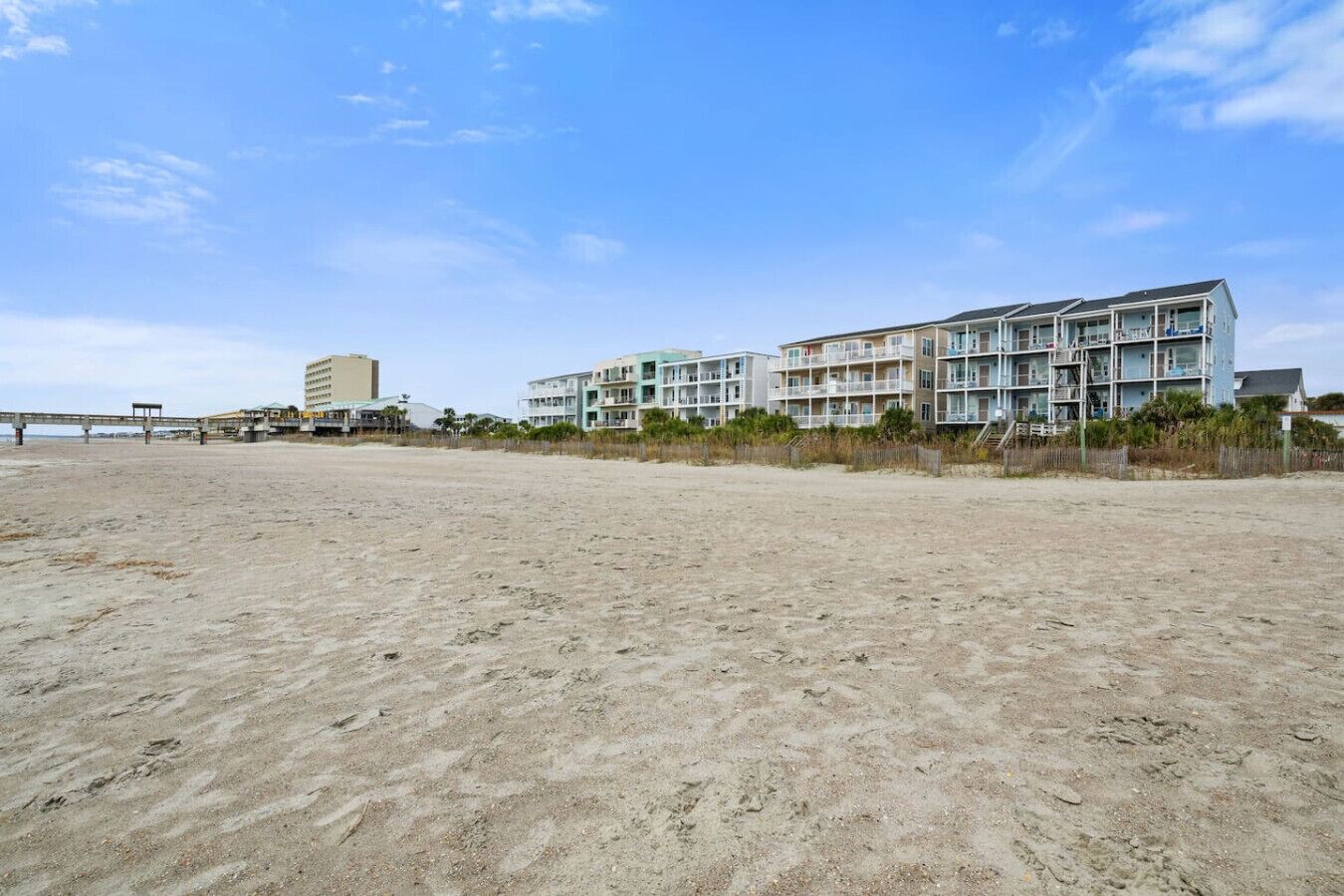 A beachside hotel with multiple balconies, a sandy beach, and a pier in the background.