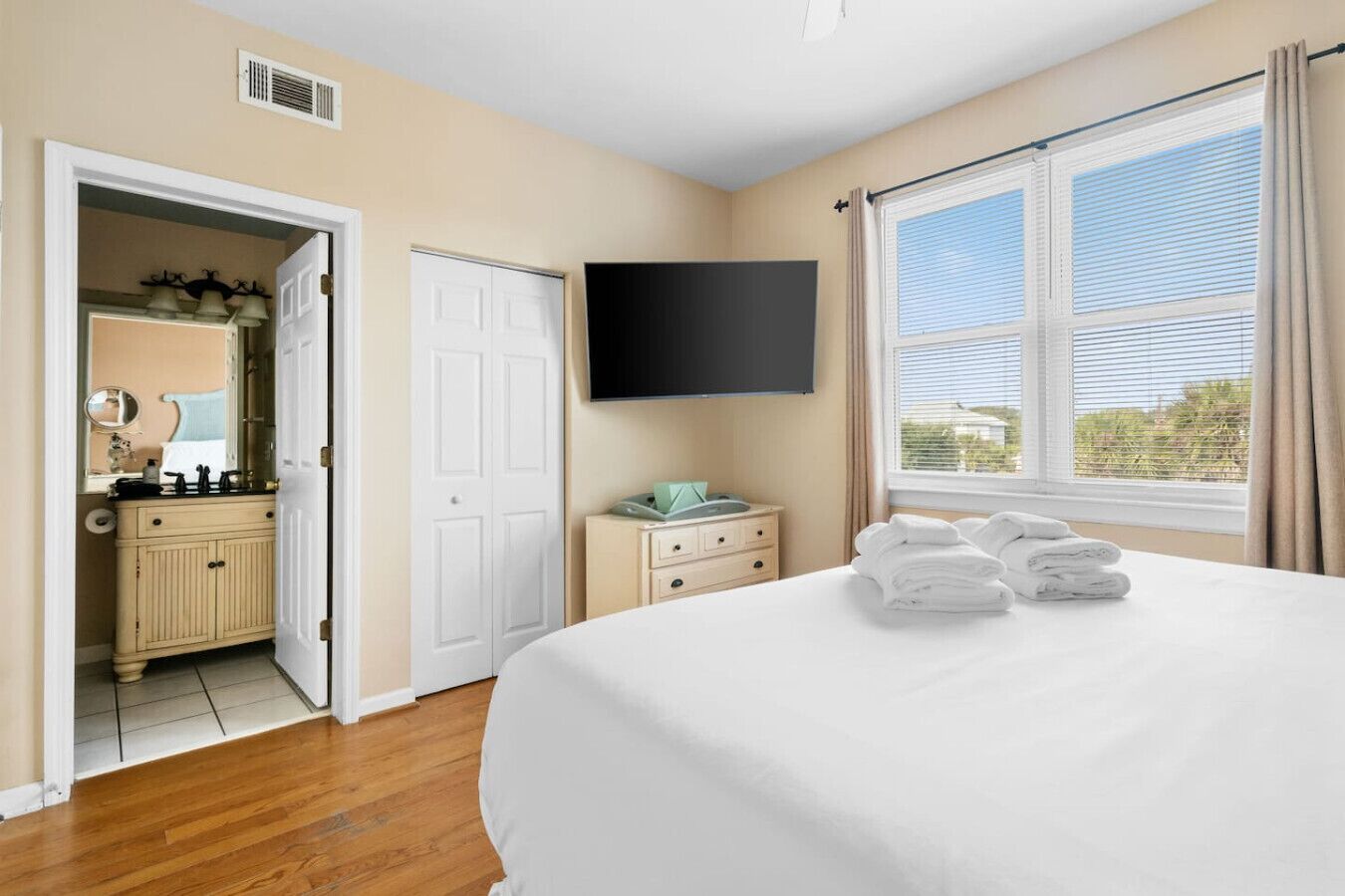 A hotel room with a bed, a TV, a bathroom with a mirror, and a window with curtains.