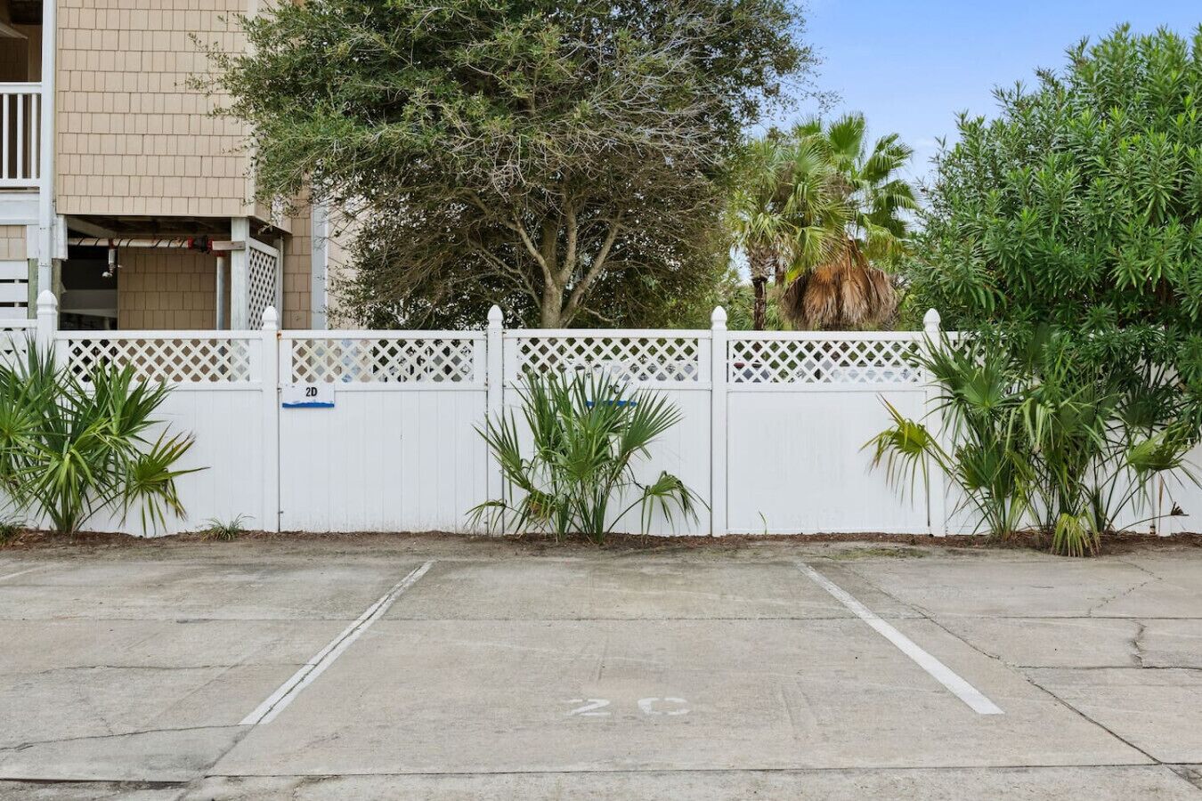 A parking area with a white fence, palm trees, and a building in the background.