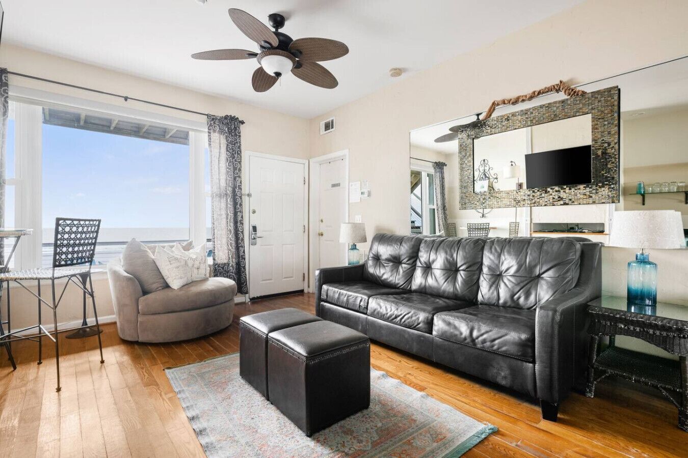 A living room with a sofa, ottoman, and a ceiling fan.